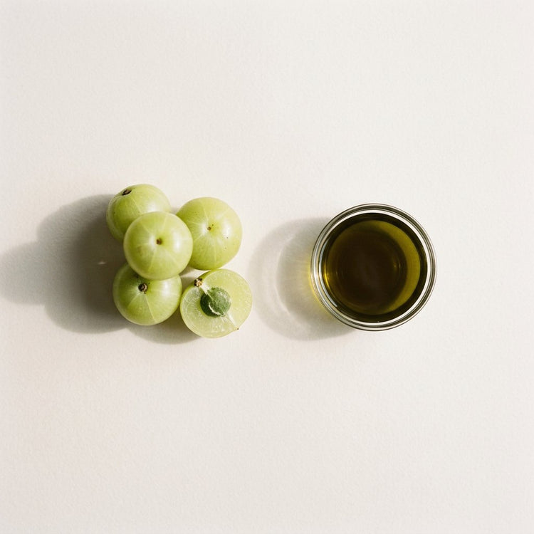 Amla (infused): amla fruits, one cut in half, beside a small glass dish of the oil.
