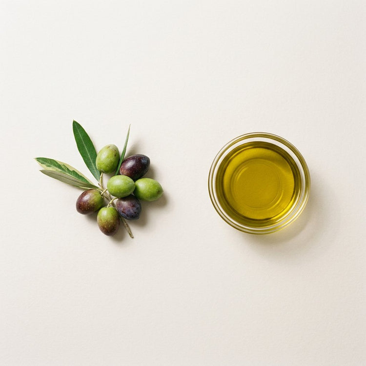 Olive: green and dark olives with olive leaves, beside a small glass dish of the oil.