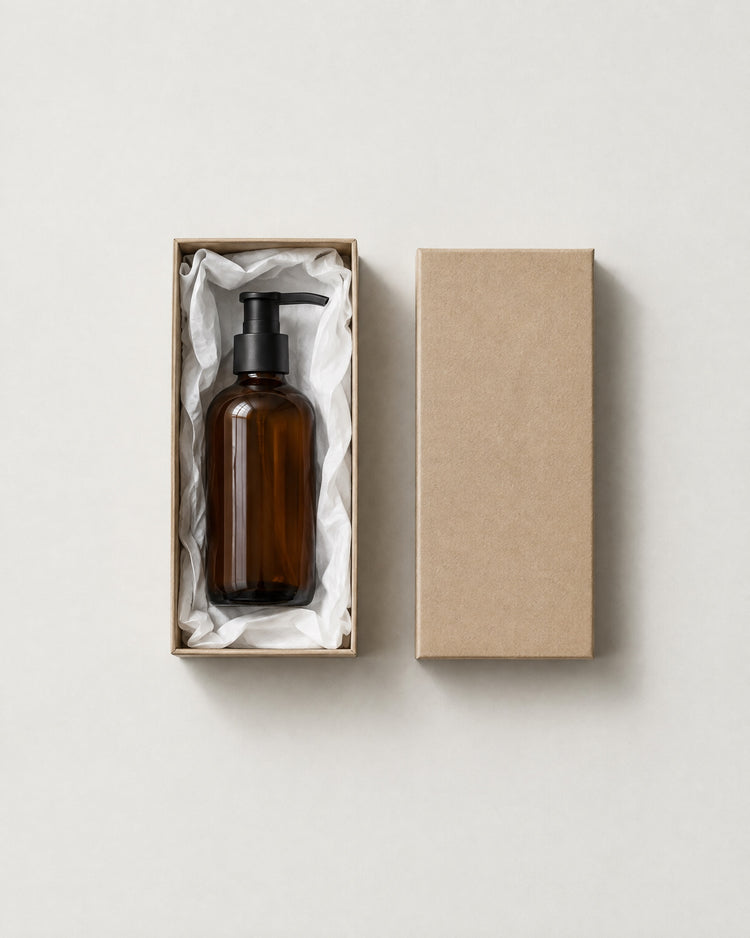 An amber pump bottle lying on white tissue in a plain kraft box, with the lid beside it.