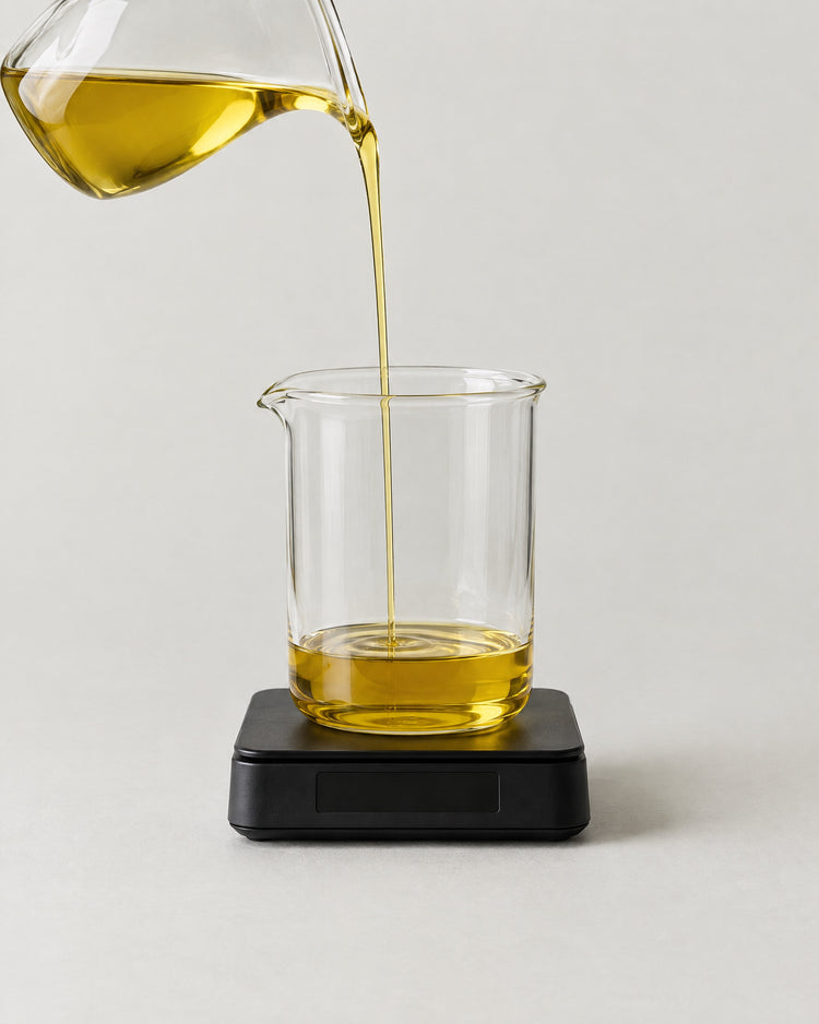 Golden oil pouring in a thin stream into a glass beaker standing on a small black scale.
