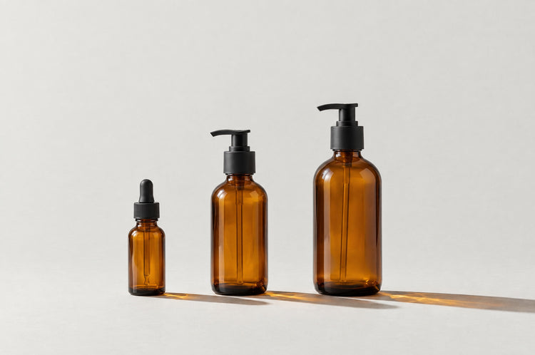 Three amber glass bottles in a row in ascending size: one with a dropper, two with pumps.