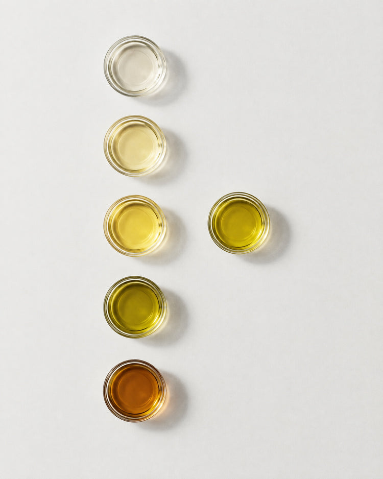 Five small glass dishes of oil in a column, graded from clear to dark amber, with one set apart.